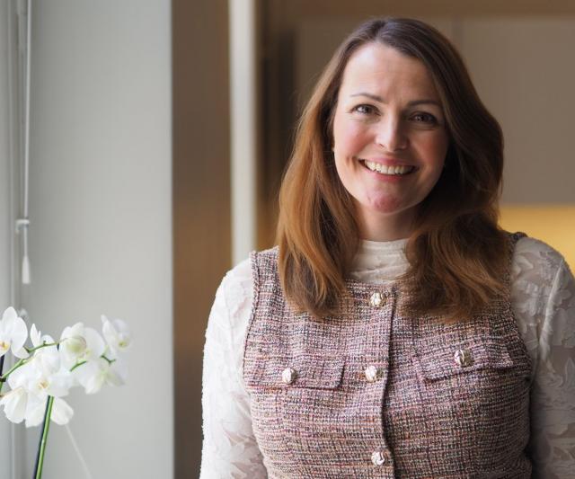 Annina Alexandersson står vid ett fönster och ler mot kameran.